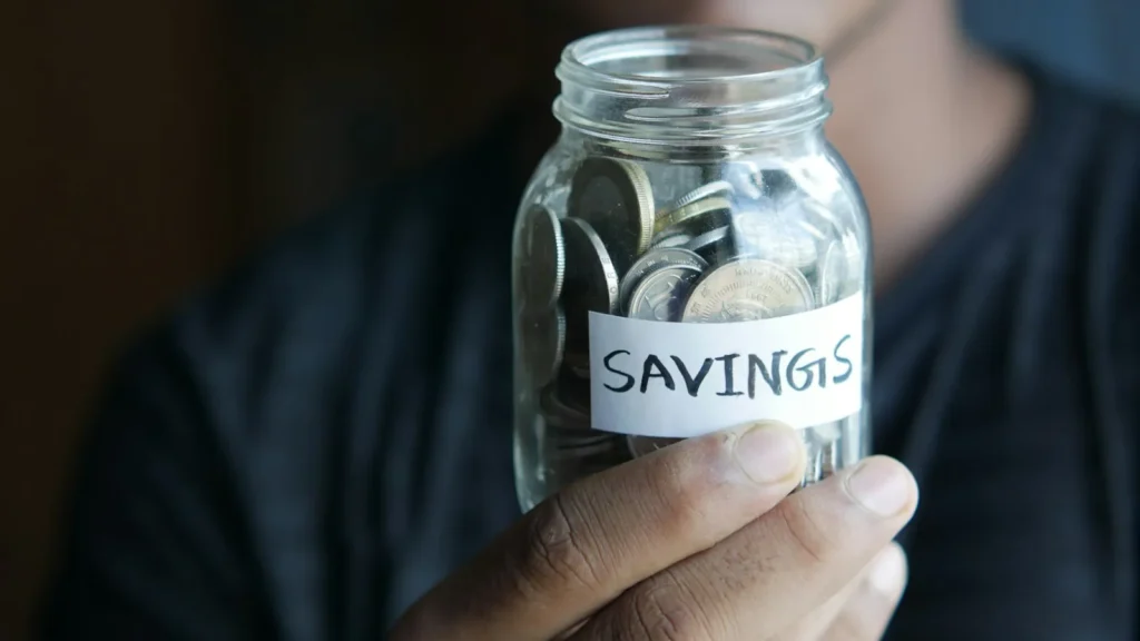 Glass jar of cash savings on a kitchen table, representing an emergency fund built step by step