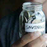 Glass jar of cash savings on a kitchen table, representing an emergency fund built step by step