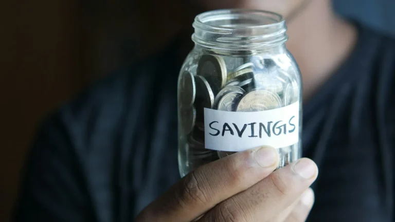 Glass jar of cash savings on a kitchen table, representing an emergency fund built step by step