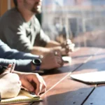 Entrepreneur writing a small business plan with charts and notes spread across a wooden desk